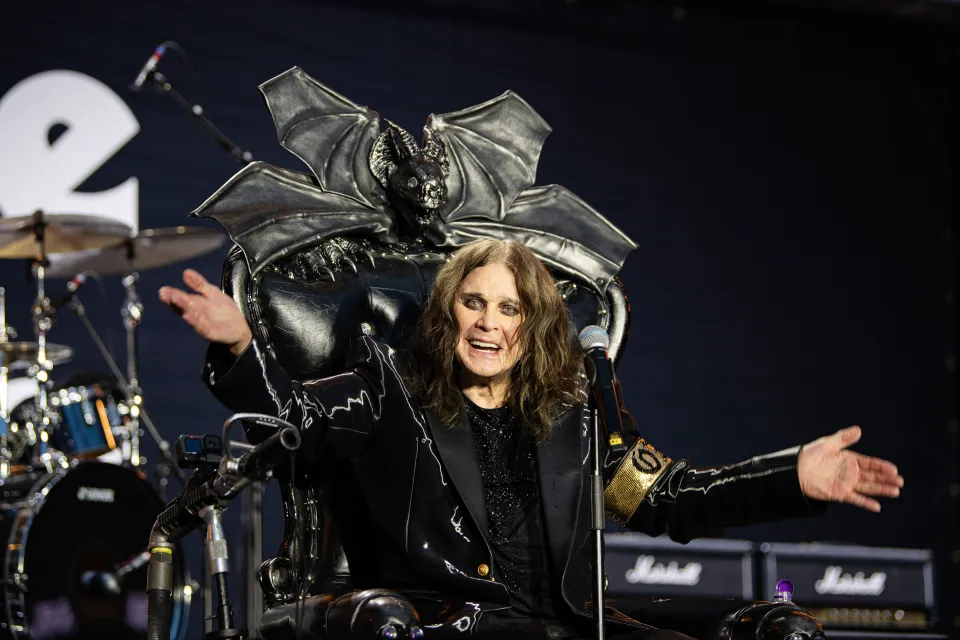 Screenshot of a performer on stage singing into a microphone while sitting on a throne.