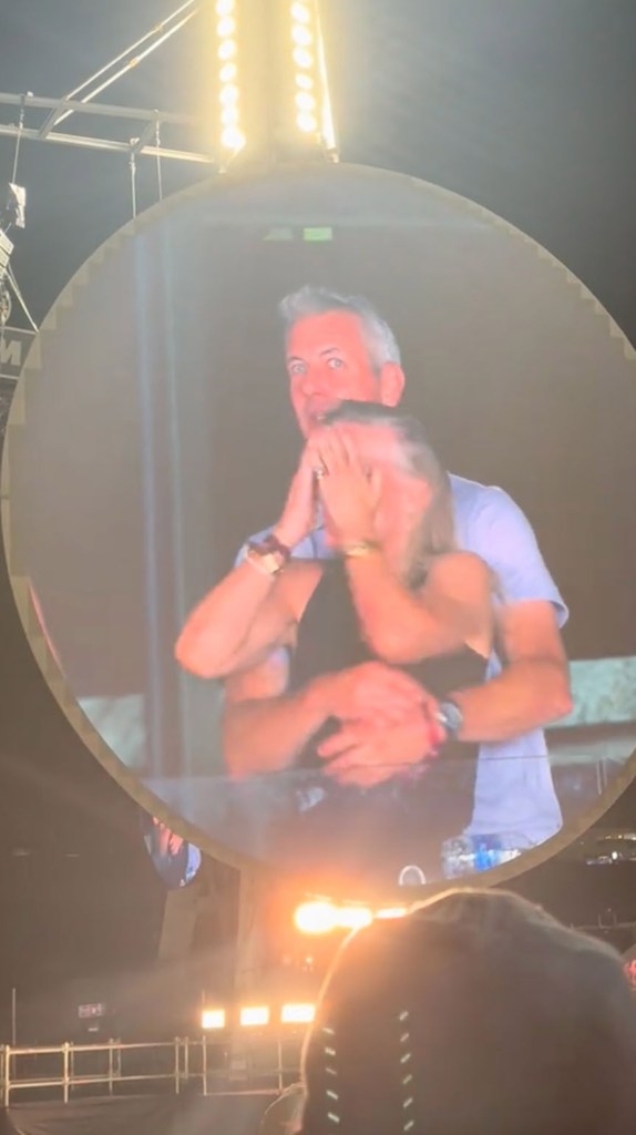 Couple embracing on a large screen at a Coldplay concert.