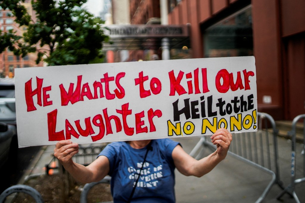 Protestor holding a sign that reads "He Wants to Kill Our Laughter Heil to the No No!" in front of the CBS broadcast center in New York City.